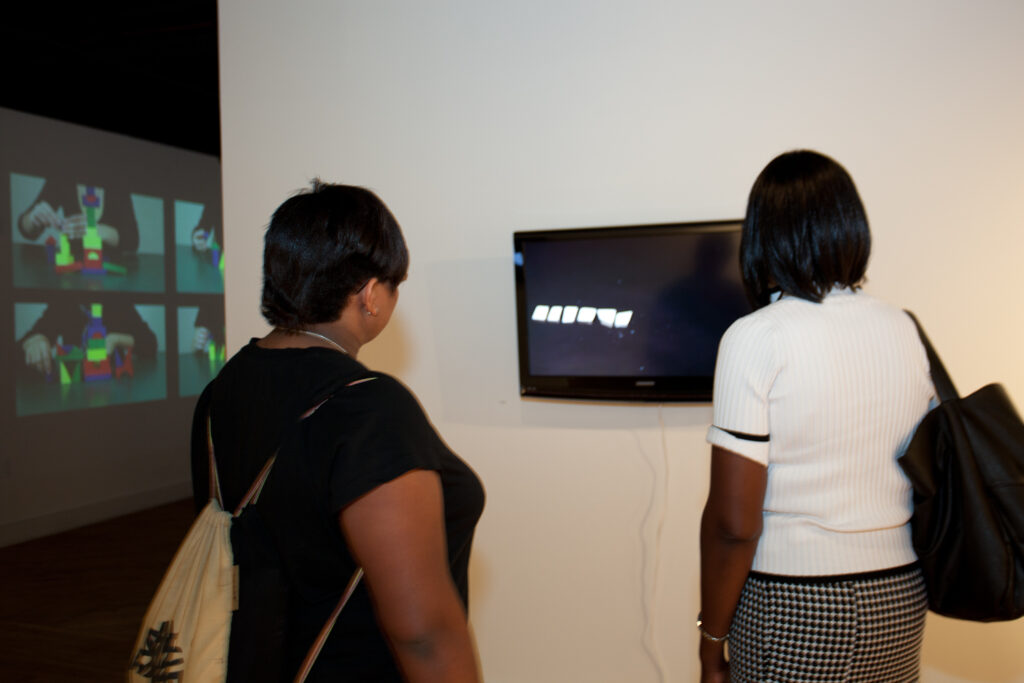 two woman standing watching a video with wall projection in background