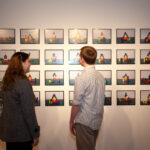 woman and man looking at grid of photographs on wall