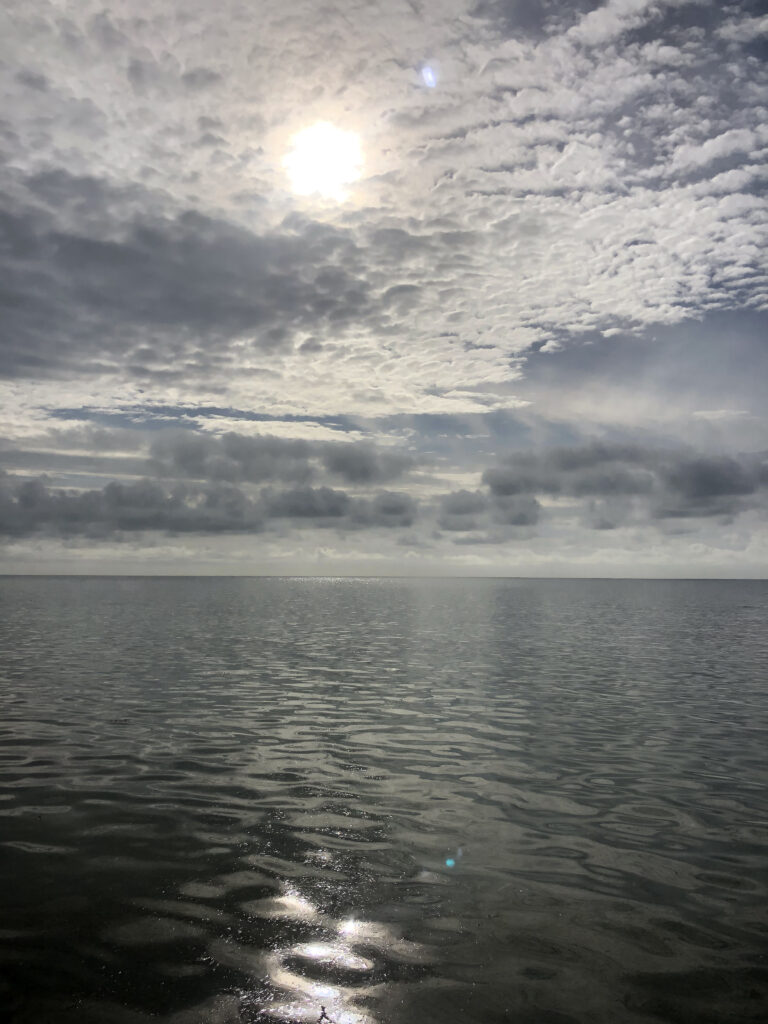 Photo by Erika Heffernan Day 266 9:23 AM at Smather’s Beach Boardwalk Key West. Vertical, Sun shining through the clouds over the ocean