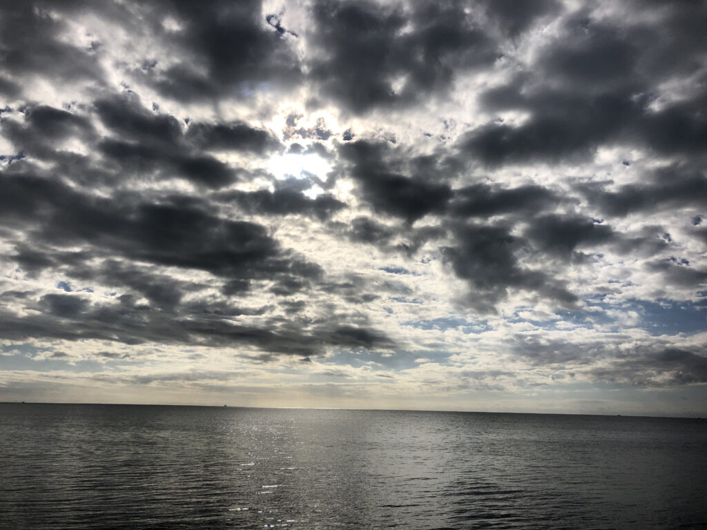 Photo by Erika Heffernan Day 288 at Smather’s Beach Boardwalk Key West. Horizontal, Field of gray Clouds fill up the whole sky with sun peeking through over the gray ocean