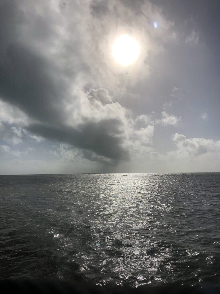 Photo by Erika Heffernan Day Day 293 9:46 AM at Smather’s Beach Boardwalk Key West. Vertical, Clouds covering a shining sun ball over the dark ocean