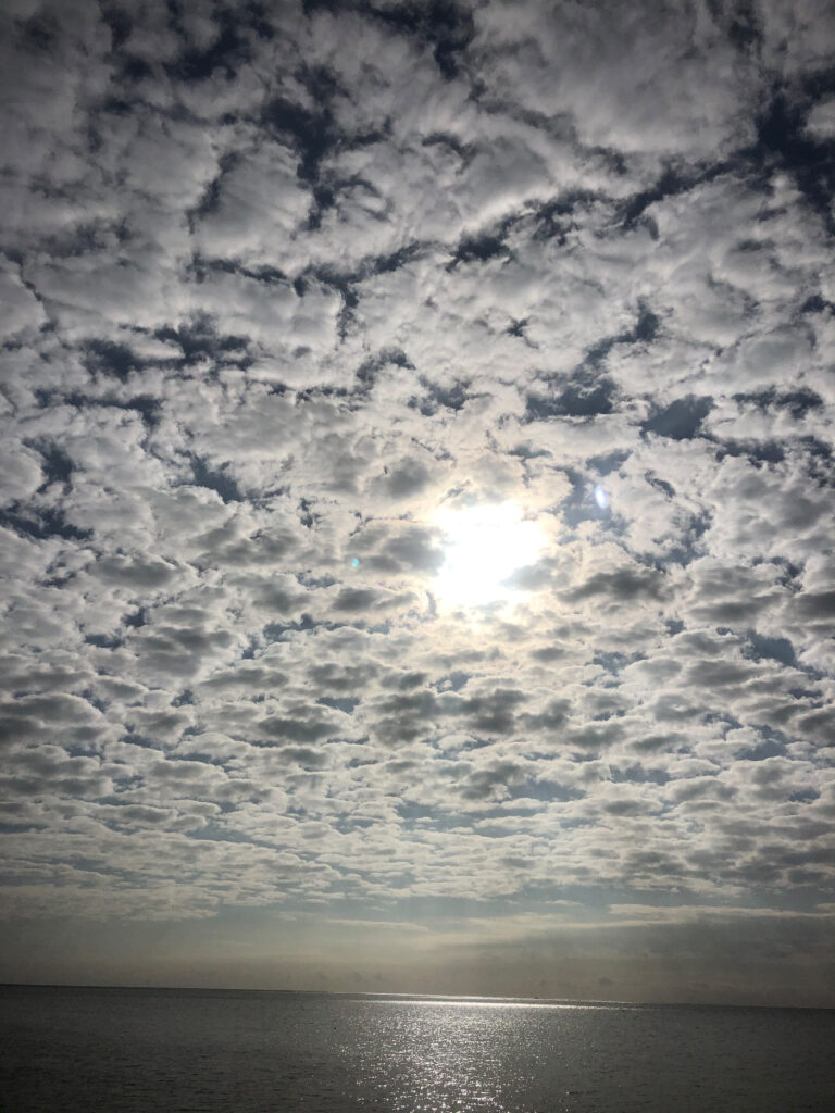 Photo by Erika Heffernan Day Day 311 at Smather’s Beach Boardwalk Key West. Vertical, cirrocumulus clouded sky with blue behind it over a thin, gray ocean with light reflections