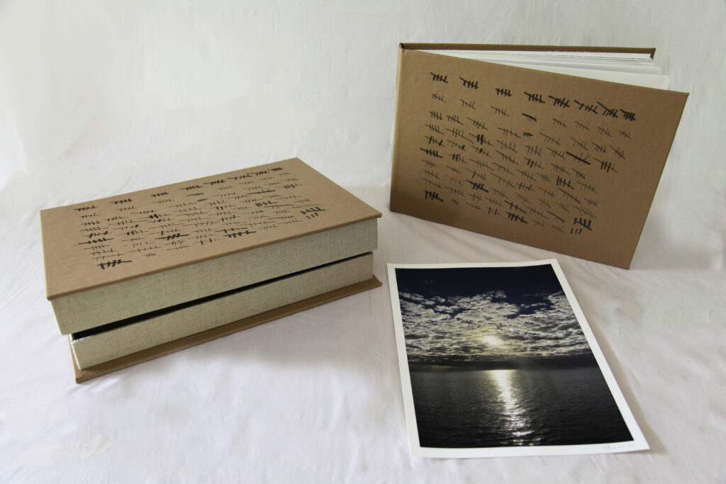 Sand Colored Leather bound Artist book with burned hash marks representing 398 Days, Clamshell box and Artist print of Sun through cloud over the ocean